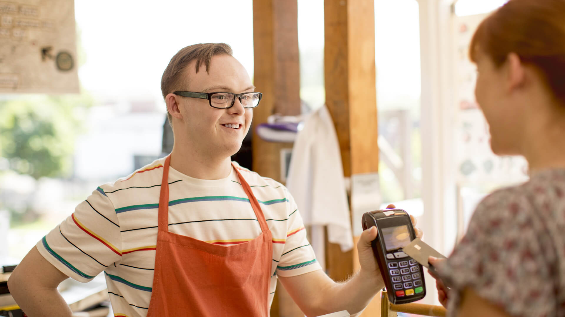 Young man working in shop shows customer payment device